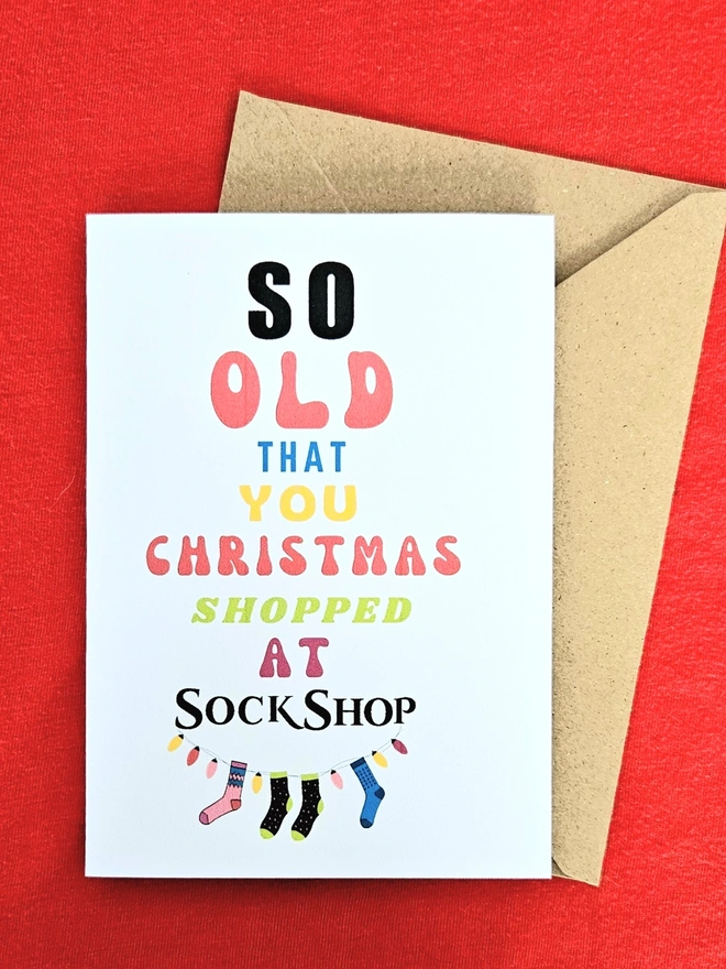 A photograph of the front of a humorous A6 greeting card illustrated using brightly coloured text and the retro shop logo. The text says so old you  Christmas shopped at Sock Shop with a brown envelope.