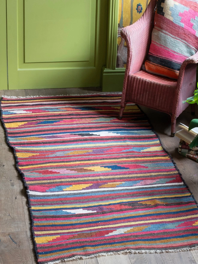 Wool vintage kilim striped rug, woven in bright colours, laid on a natural wooden floor in a room with green walls
