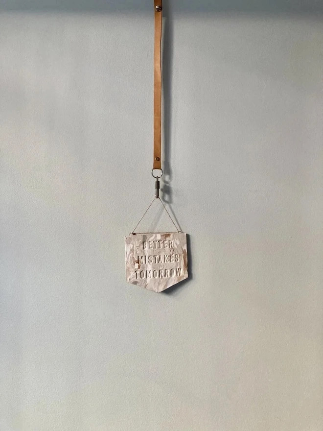 'Better Mistakes Tomorrow' Banner, a clay banner hanging against a plain backdrop.
