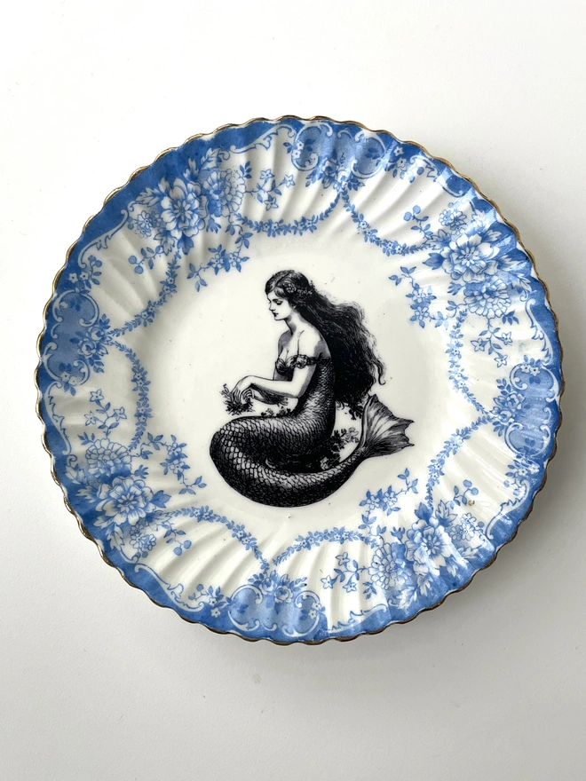 vintage plate with an ornate border, with a printed vintage illustration of mermaid in the middle 