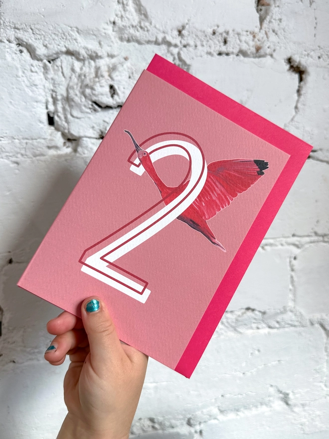 a pink card with a big white number 2 and an illustration of a scarlet ibis with a neon pink envelope