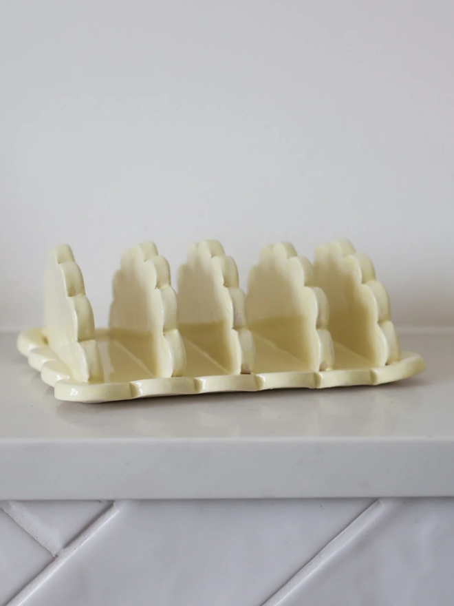 scalloped stoneware toast rack. a yellow rack for toast with scalloped edges.