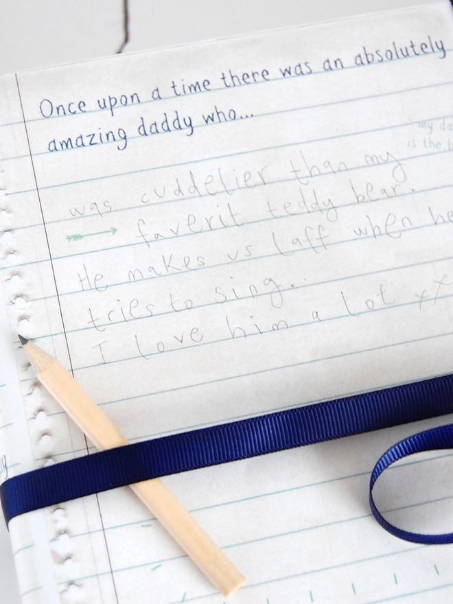 A gift wrapped in Daddy story wrapping paper, with spaces for children to write their own story to Daddy, is tied with a blue ribbon with a small pencil tucked in.