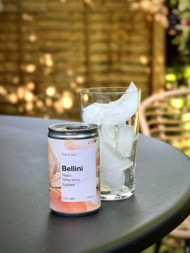 Can of Bellini on a table outside with a glass full of ice behind it