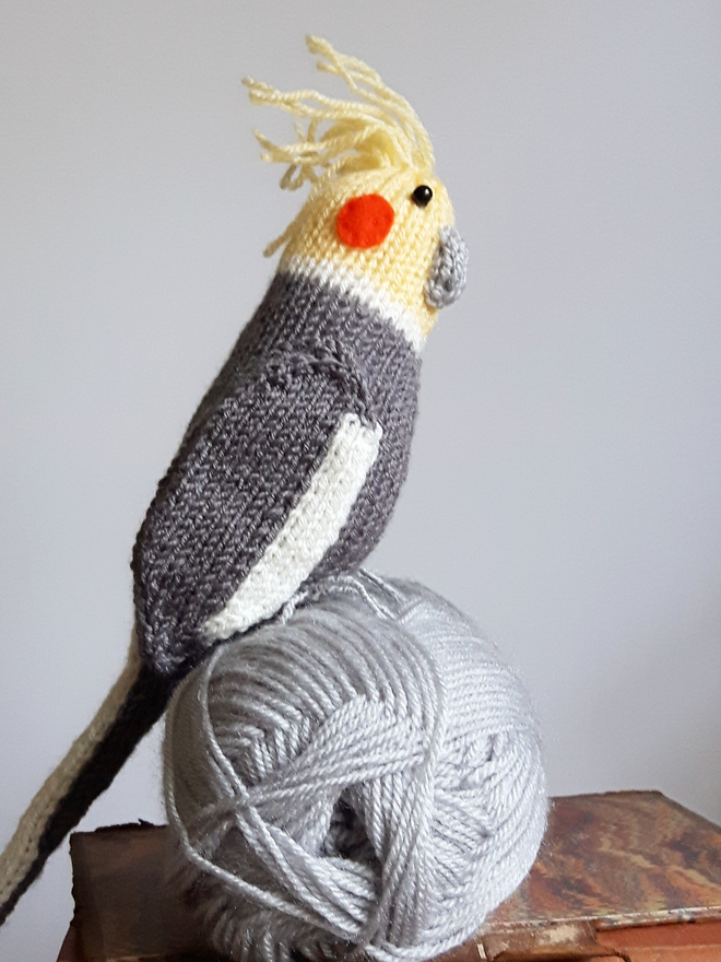 a knitted cockatiel sitting on top of a grey ball of yarn