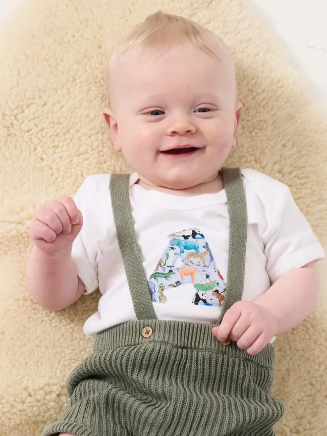 A smiling new baby wearing a bodysuit with his initial on the front cut from Liberty zoo animal print
