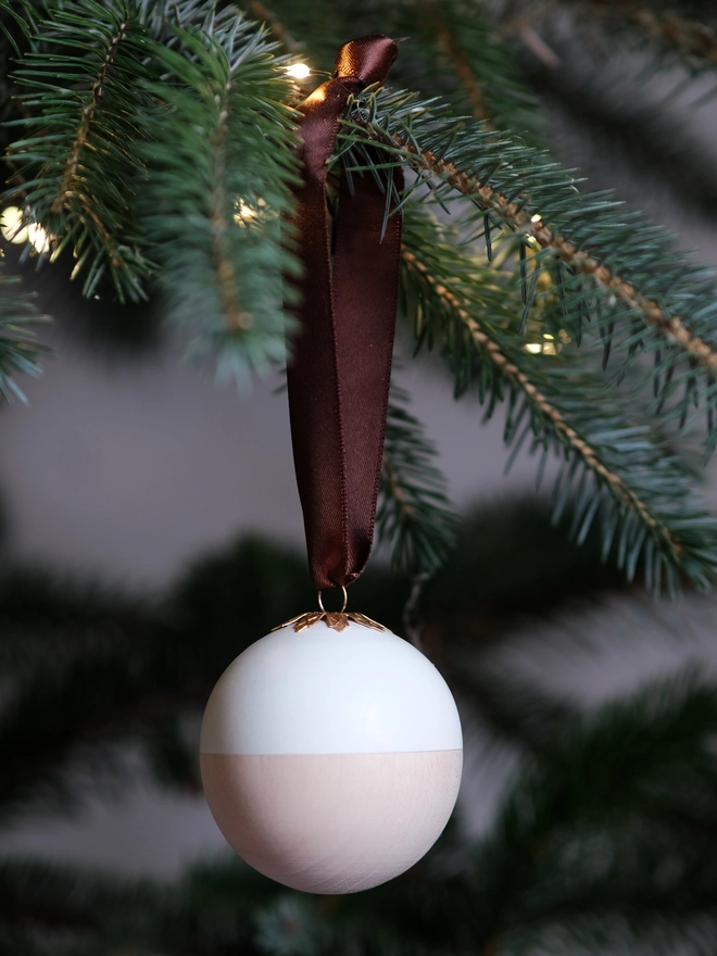 Wooden and white Christmas gift bauble with a removable lid, hanging from a Christmas tree with a space inside for a handwritten message, gift or surprise