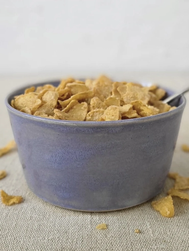 Classic Ceramic Breakfast Bowl, a breakfast bowl sitting on a grey carpet against a plain backdrop. It is accompanied by some cereal and a spoon. 