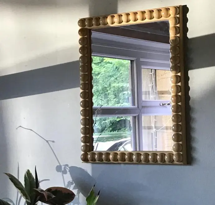 Over-sized bobbin mirror with a decorative turned-bead frame placed in a bedroom interior.