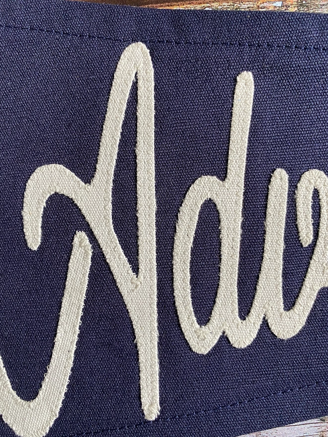 Detail of a navy canvas 'Seek Adventure' pennant flag showing the letters adv in ivory canvas