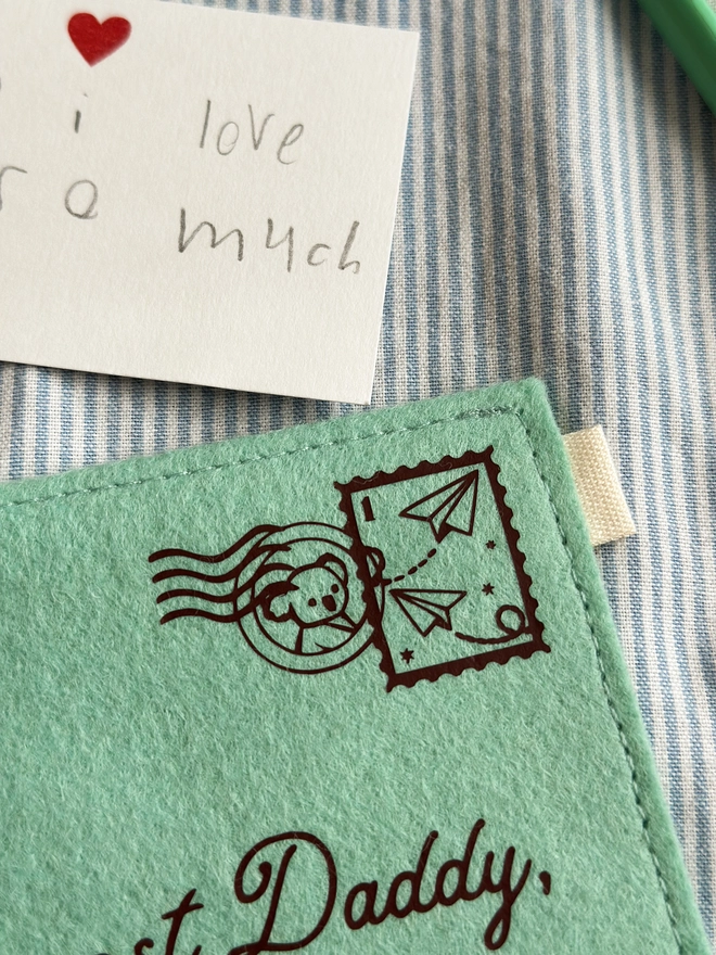 The corner of a handmade green felt envelope with a paper aeroplane stamp and a koala postmark in the top right hand corner.
