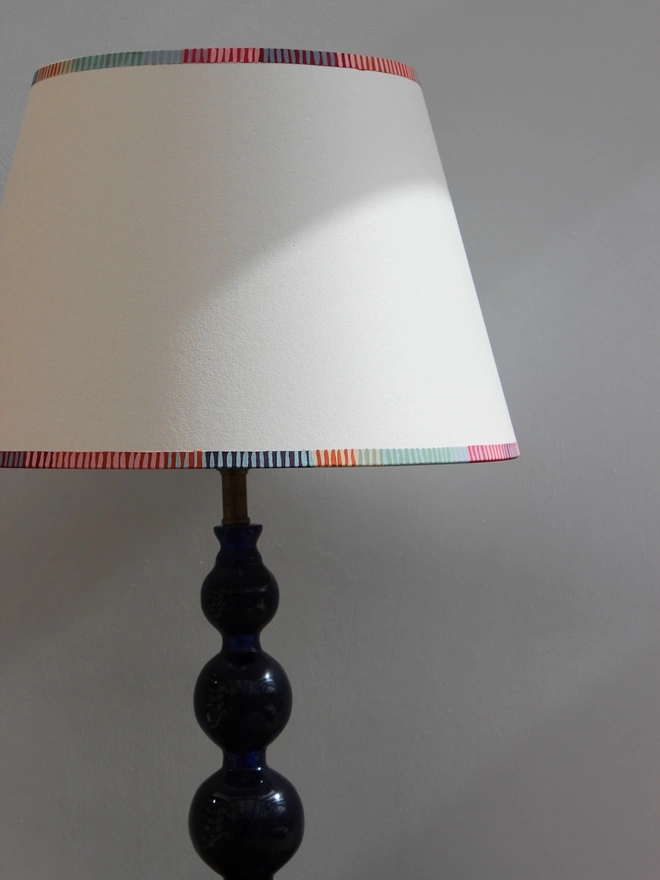 A bold lampshade with striped detailing in multiple colours, part of Studio Zef’s empire shades for table lamps collection. This striped lighting design makes a subtle but stylish statement.