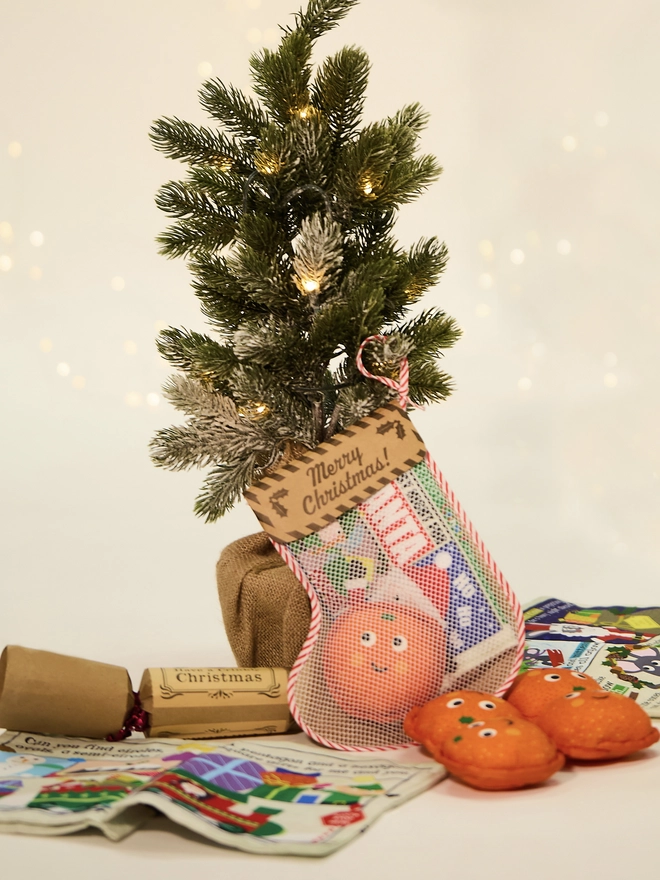 Stocking with newspaper and squishy orange toys and a cracker beside a little Christmas tree