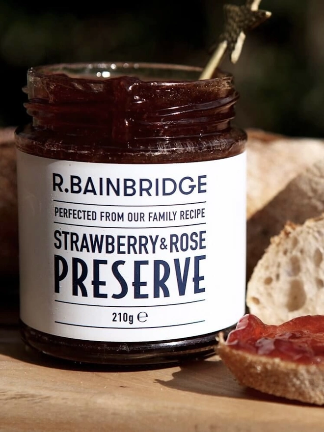 Strawberry & Rose Jam (Set Of 1, 2 Or 3), a jar of jam sitting on a wooden surface next to some toast. 