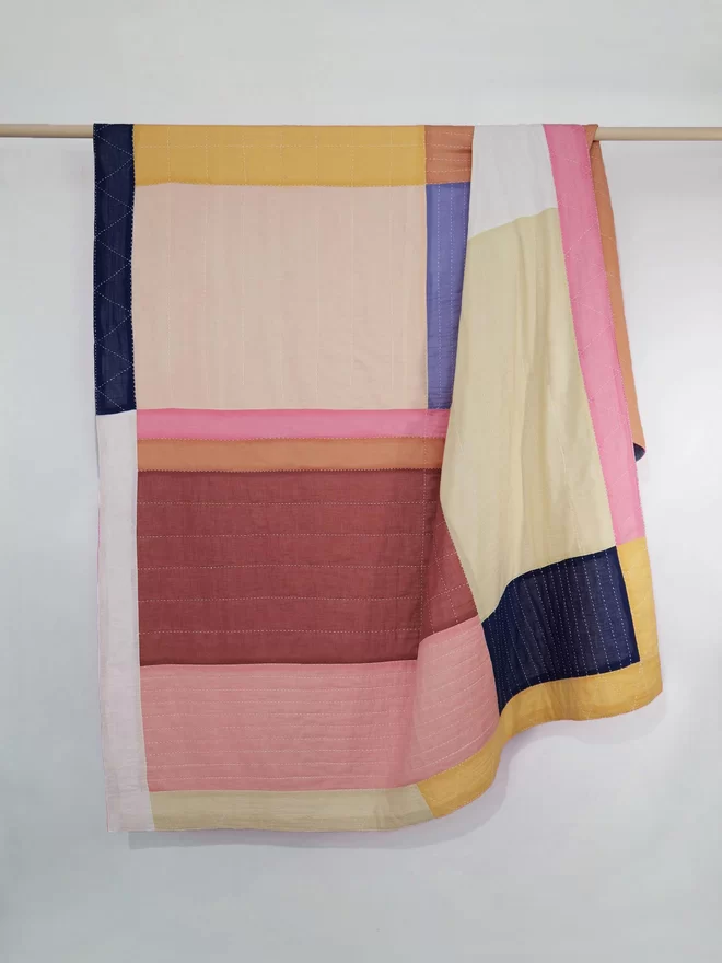 Patchwork quilt in pastel colours hanging over a wooden pole