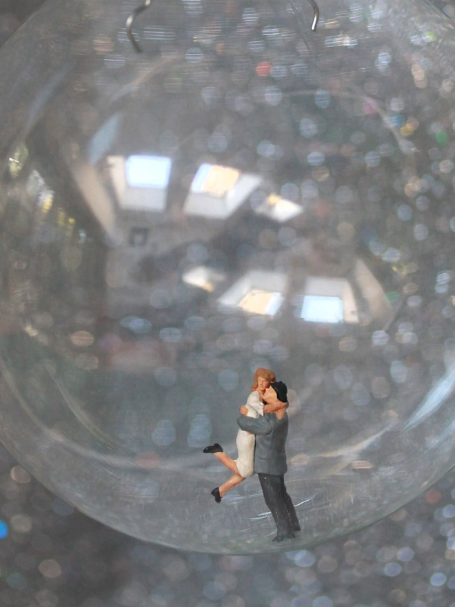Miniature figure of a hugging couple in a glass Christmas bauble - close up 