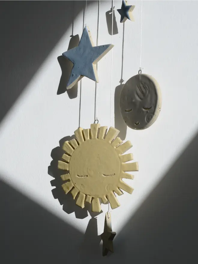 Close up of soft yellow, blue and white ceramic sun, stars and moon decorations in beam of light on dark wall