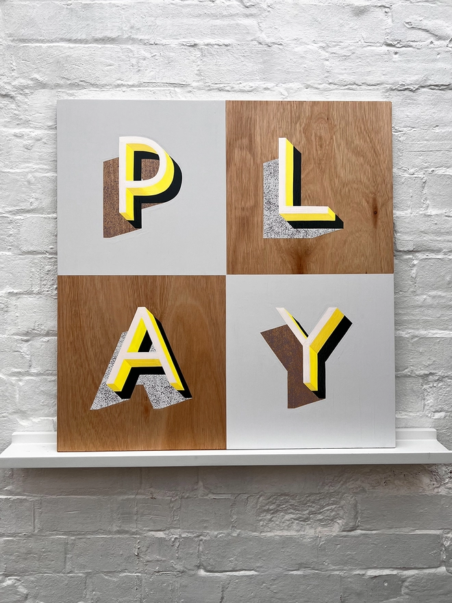 PLAY hand painted sign in neon yellow, lilac and grey, against a white brick wall, straight on. 