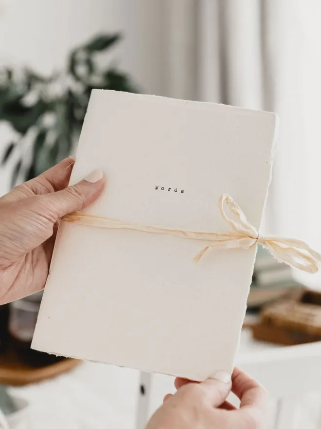 an off white journal with a deckled edge and rustic ribbon closure the word 'words' has been typed on the cover