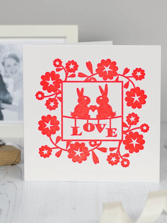 Letterpress lovebunnies card placed on table with wedding photo in background