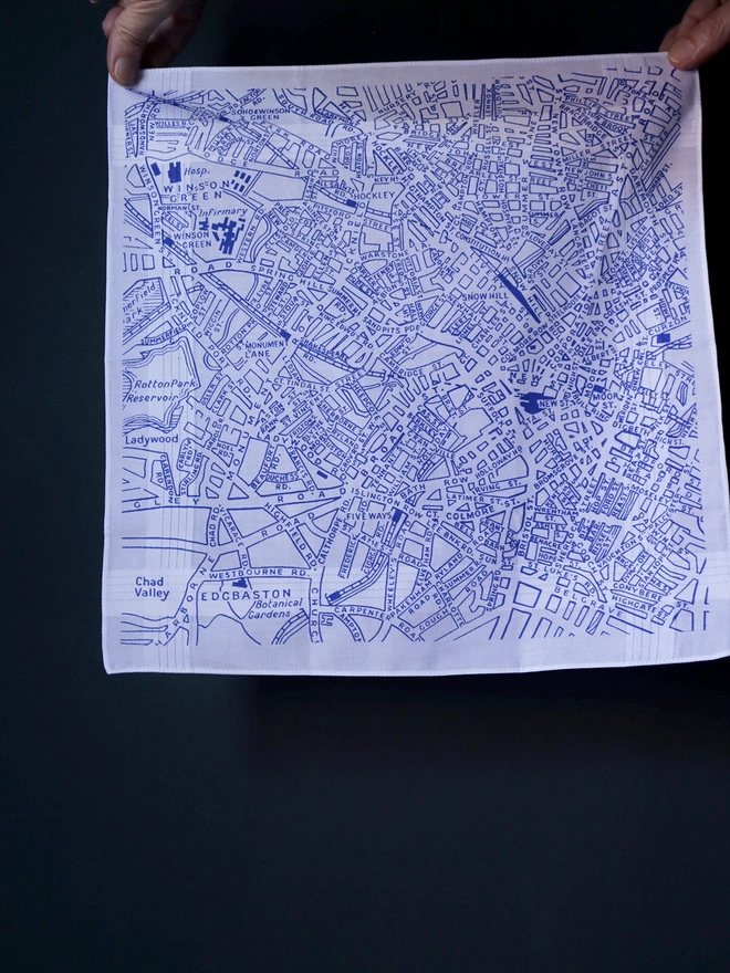 A Mr.PS Birmingham map hankie printed in classic blue held aloft by two hands in front of a dark wall 