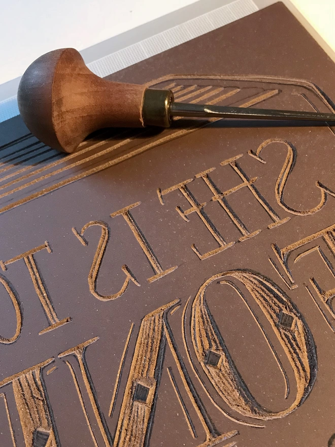 linocut block showing carved lettering and wooden handled lino cut tool