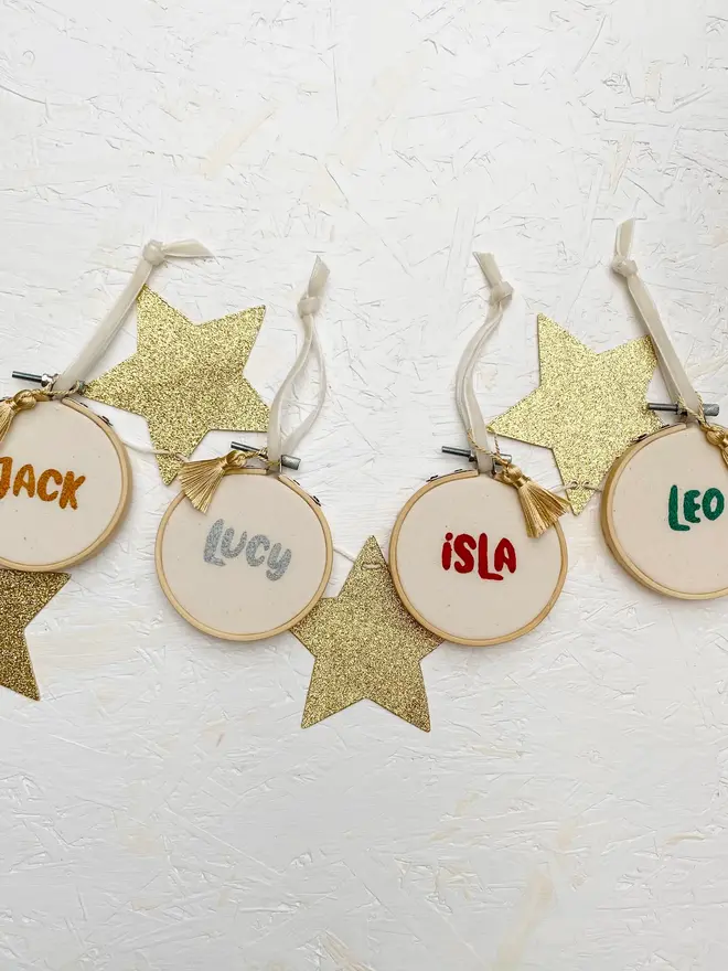personalised name embroidered hoop bauble. set of 4 embroidered hoop baubles strung up on white wall.