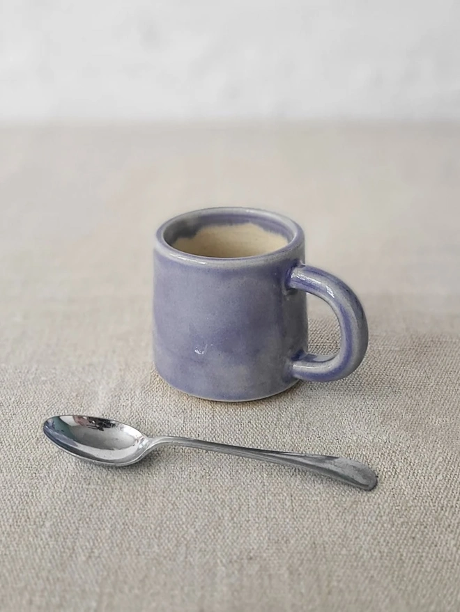 Classic Ceramic Espresso Mug, a colourful ceramic espresso mug sitting on a plain surface against a white backdrop. It is accompanied by a spoon. 