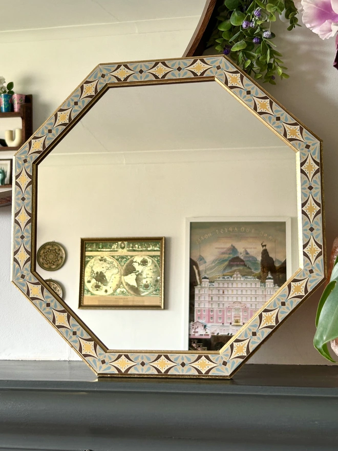 Medium sized octagonal wall mirror with a hand painted decorated frame with gold stars and blue star burst repeating pattern around the frame