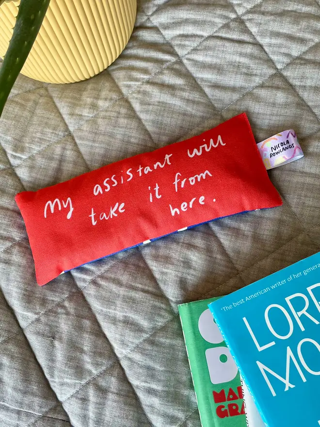 Red lavender eye bag lies on a bed next to a pile of books