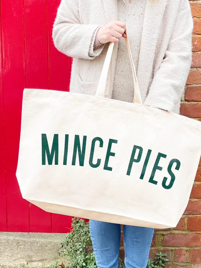 model carrying an oversized natural canvas tote bag with bold mince pies slogan