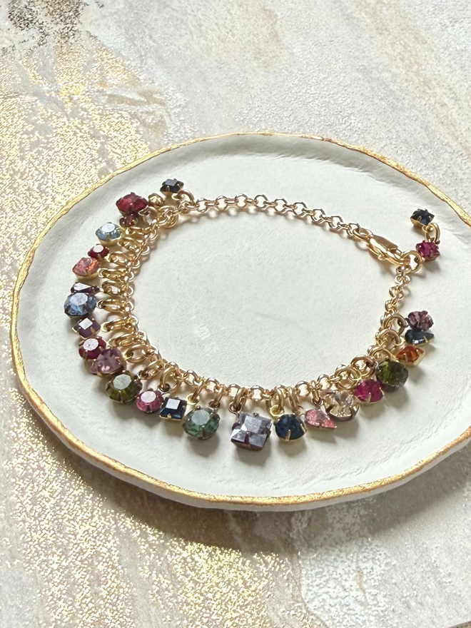 golden chain bracelet with rainbow jewel charms sitting on white dish