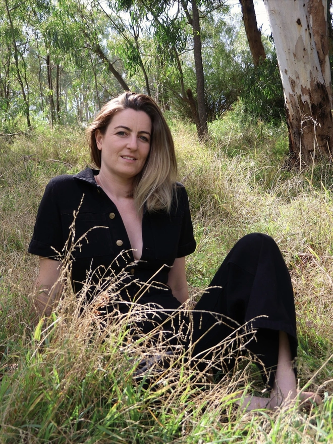 Woman sitting in grass wearing black jumpsuit