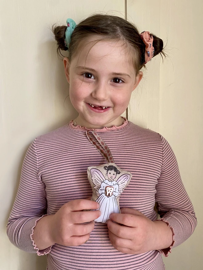 a little girl with a missing tooth holding a tooth fairy decoration 