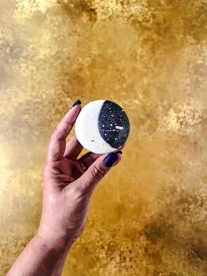 a person holding a macaron decorated like a moon with a starry night sky background l in front of a gold background