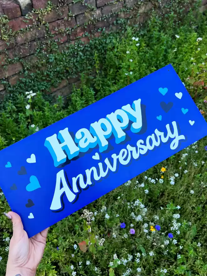 'Happy Anniversary' on a blue background with white lettering, blue shades and heart details.