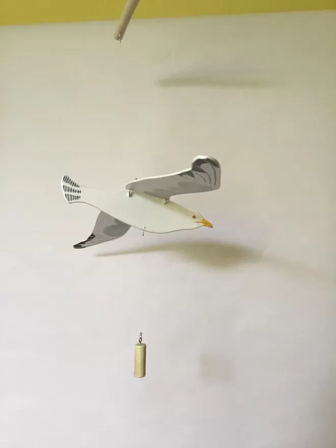 Flying wooden seagull hanging from ceiling against a white wall 