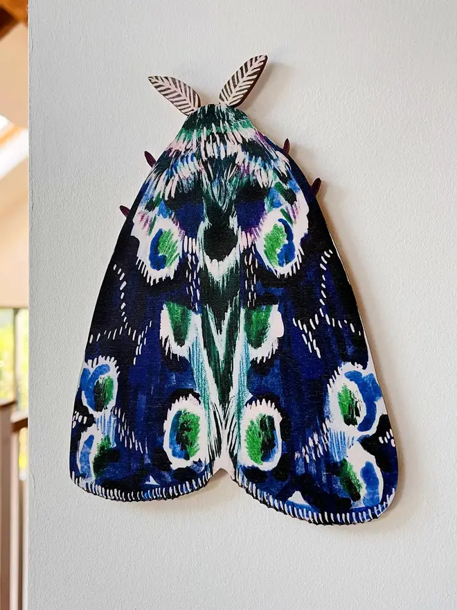 large wooden moth wall decoration. large blue wooden moth decoration hung on plain white wall.