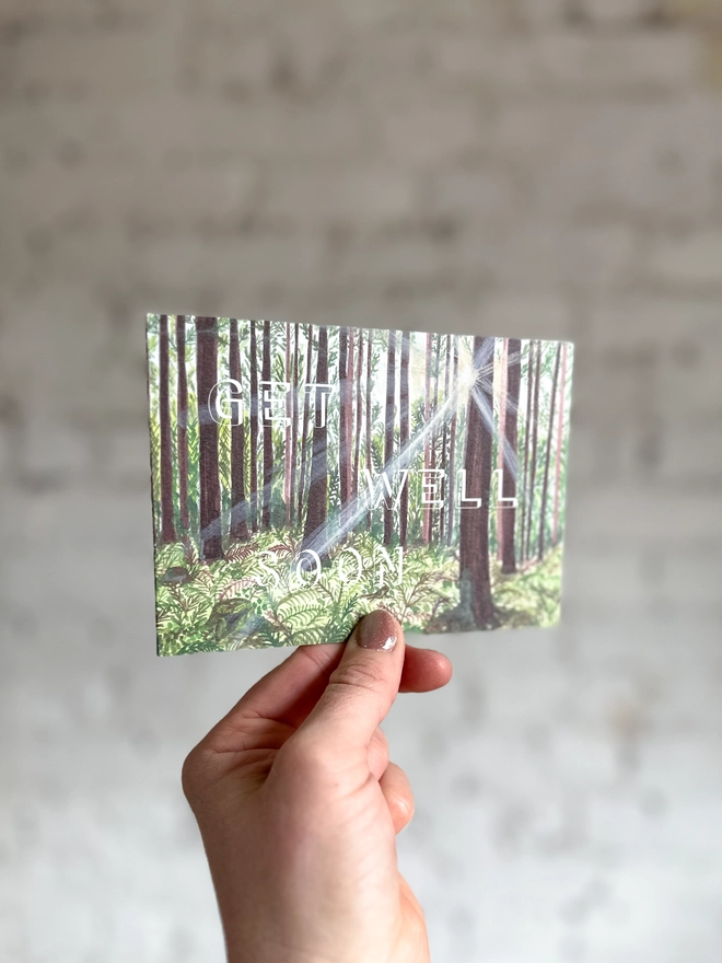a greetings card featuring an illustration of a woods landscape with the text “get well soon”