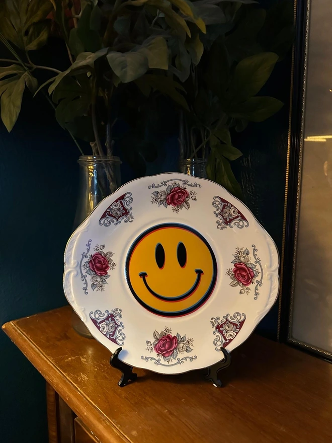 A round plate with a border of roses and a yellow smiley face in the center