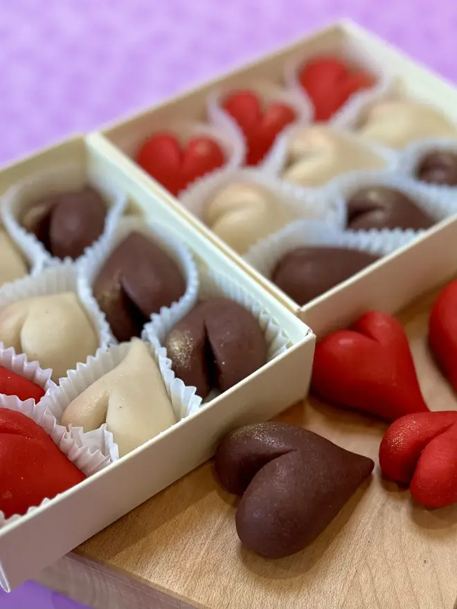 Marzihearts Valentines Chocolates (Box Of 6, 9, 12), two boxes of valentines chocolates on a wooden chopping board. The cherry, chocolate and marzipan chocolate hearts sit in front of a purple background. 