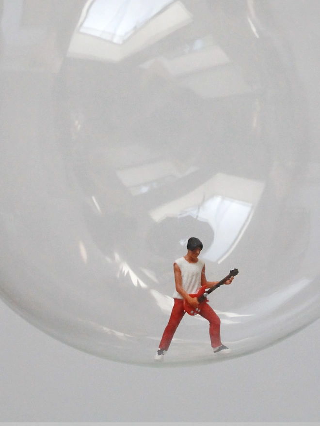 Miniature figure of a guy playing an electric guitar in a glass Christmas bauble - close up 