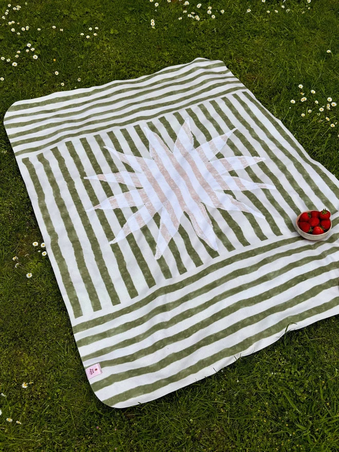 sun stripe fleece blanket. a green and white striped picnic blanket on grass.