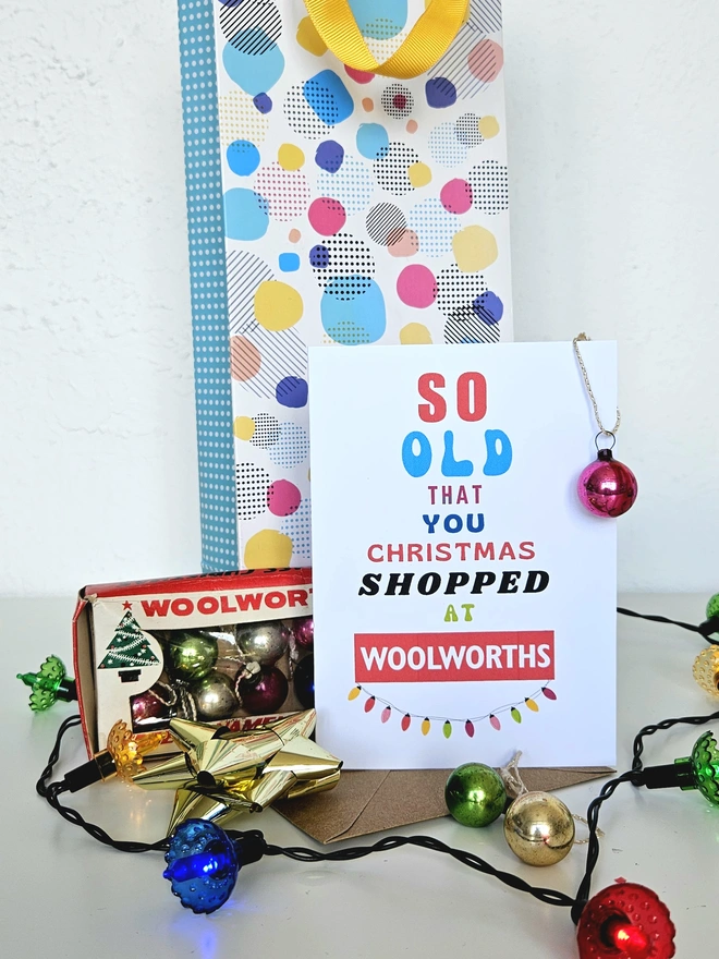 A photograph of the front of a humorous A6 greeting card illustrated using brightly coloured text and the retro shop logo. The text says so old you Christmas shopped at Woolworths with string lights