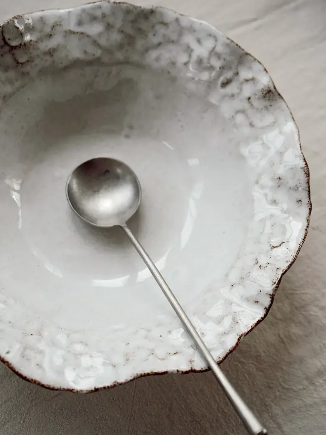 Dapple Stoneware Cereal & Salad Bowl, with a spoon, placed on a table cloth. 