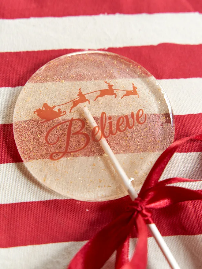 Large sparkly Believe Lollipop placed on a red striped tablecloth