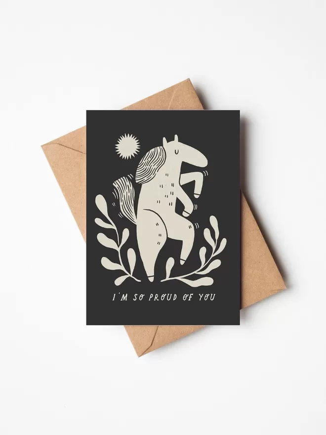 Black and white greeting card with illustration and the words I'm so proud of you written on it with a brown envelope underneath it