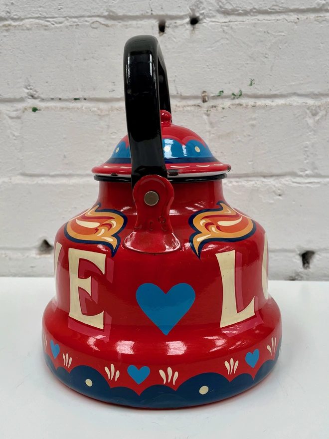 Red vintage enamel kettle, hand-painted with a fairground inspired design in orange, pink, yellow and blue. 'Love' is painted in large lettering across the centre.