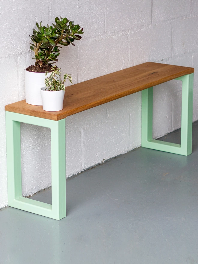 oak bench with chunky box section steel legs in pistachio green, set against a hallway wall with pot plants at one end.