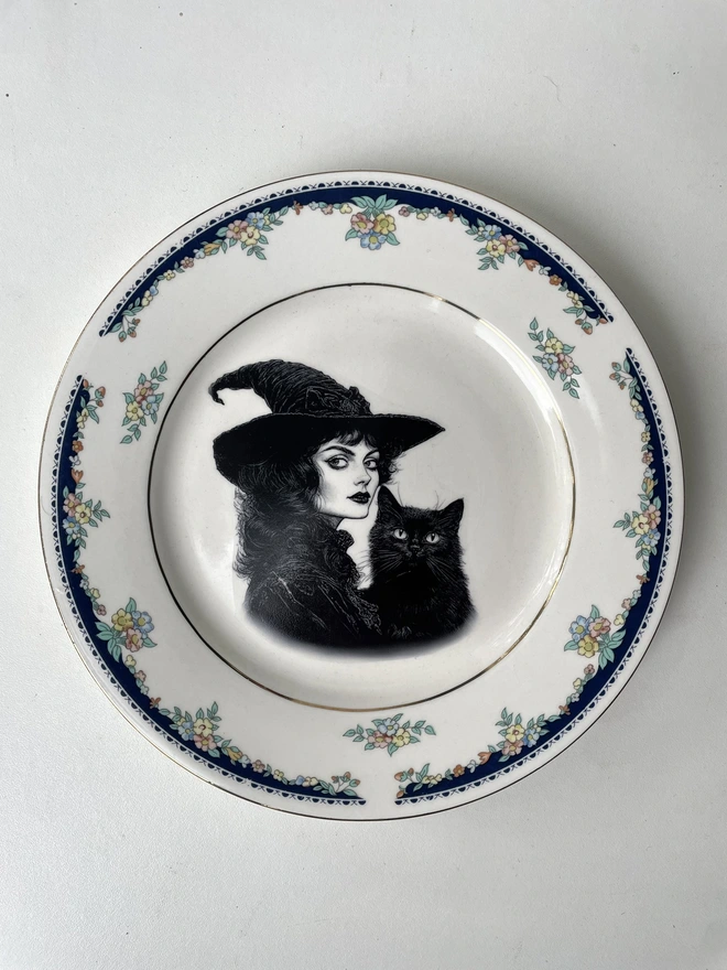 vintage plate with an ornate border, with a printed vintage illustration of a Victorian witch and her black cat in the middle